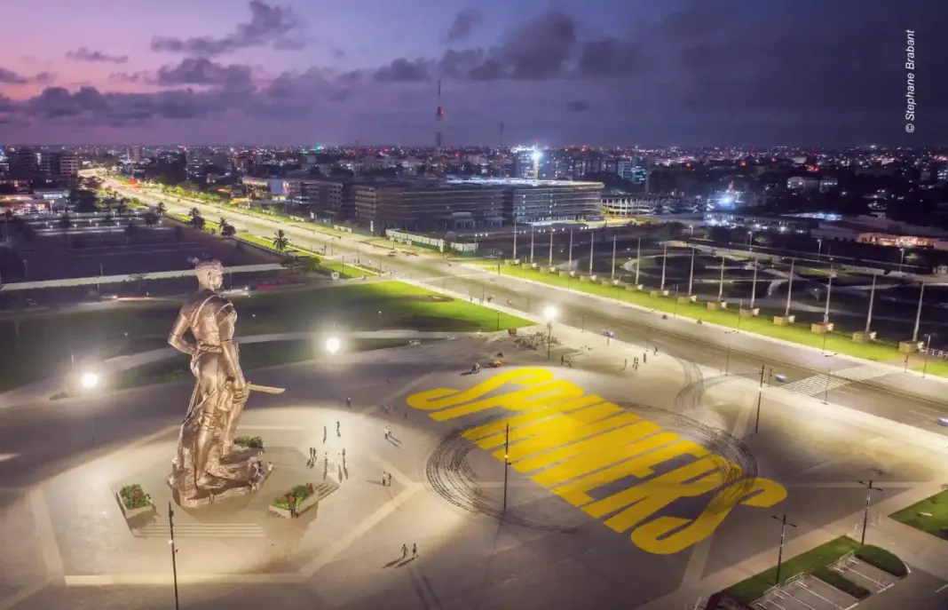 Image de Société. La mystérieuse apparition de marques de pneus et de tags jaunes vifs à la Place de l’Amazone à Cotonou a captivé l'attention des passants, suscitant curiosité et spéculations. Ces signes énigmatiques ne sont pas le fruit du hasard, mais les prémisses d'un événement sensationnel qui promet de révolutionner le paysage urbain : l'arrivée imminente du spectacle de « Spinners ». Si vous avez récemment arpenté la plus grande esplanade du boulevard de la Marina, vous avez probablement été intrigué par ces traces de pneus inhabituelles qui s'étendent sur le béton, accompagnées d'un tag jaune vif portant l'inscription « spinners ». Cet affichage spectaculaire est bien plus qu'une simple manifestation artistique urbaine ; c'est une stratégie de marketing immersive pour annoncer la sortie imminente d'une série télévisée révolutionnaire. Le phénomène s'étend au-delà des frontières de Cotonou, avec des signes similaires repérés dans des endroits emblématiques de grandes métropoles africaines telles que le cinquième pont Alassane Ouattara à Abidjan, l'échangeur Joss à Douala, le carrefour Rio à Libreville, et même à Kinshasa. Ces marques de pneus sinueuses racontent une histoire fascinante de vitesse, de contrôle et d'art, préfigurant l'arrivée imminente du Spinning dans ces villes. Le Spinning, une forme audacieuse de sport automobile où les conducteurs exécutent des cascades et des drifts spectaculaires, a déjà gagné en popularité dans les townships du Cap en Afrique du Sud. À présent, cette discipline à couper le souffle débarque au Bénin, apportant avec elle une vague d'adrénaline et de performances techniques. CANAL+, la chaîne de télévision de renom, a choisi de célébrer cet événement en lançant une nouvelle création originale intitulée « Spinners ». Cette série promet de plonger les téléspectateurs dans l'univers palpitant du Spinning. L'histoire suit Ethan, un jeune homme de 17 ans dont la vie est marquée par la violence des gangs. À travers le Spinning, il découvre un exutoire, une manière de transcender les défis de son environnement et de protéger son petit frère. Le lancement officiel de la série est prévu pour le 13 novembre 2023 sur CANAL+ PREMIERE. Chaque soirée sera marquée par la diffusion exclusive de deux épisodes inédits, promettant de tenir en haleine les amateurs d'action et d'émotions fortes. Ainsi, les marques de pneus et le tag jaune qui ont émergé de manière énigmatique à la Place de l’Amazone ne sont pas simplement des empreintes, mais plutôt les prémices d'un phénomène qui va secouer les rues de Cotonou et au-delà. L'art du Spinning, avec ses traces distinctives, est sur le point de conquérir le paysage urbain, transformant l'ordinaire en extraordinaire. Alors que l'excitation monte à l'approche du lancement de « Spinners », les rues résonneront bientôt des rugissements des moteurs et des acclamations des spectateurs, prêts à être emportés par cette nouvelle vague de divertissement sensationnel. La question demeure : comment cette série révolutionnaire va-t-elle redéfinir le paysage audiovisuel et la culture urbaine au Bénin et au-delà ?